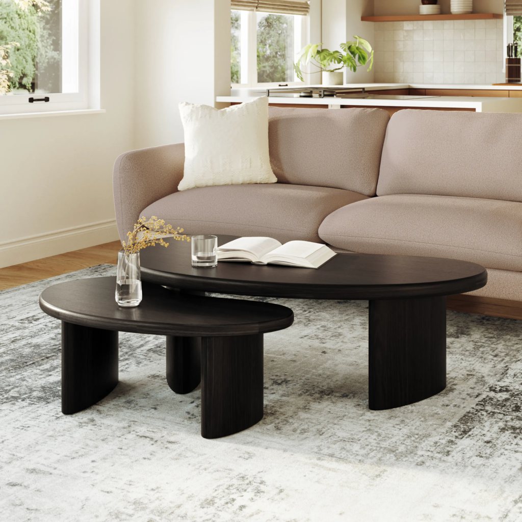 Black nesting coffee tables with curved tabletops in front of a neutral sofa.