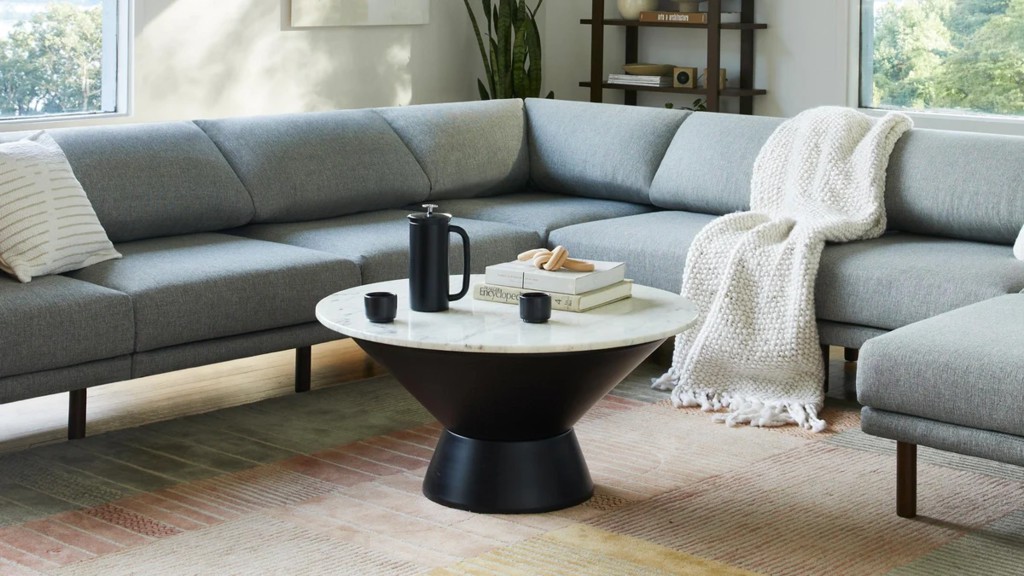 Gray U-shaped sectional sofa with a round marble coffee table in a bright living room.