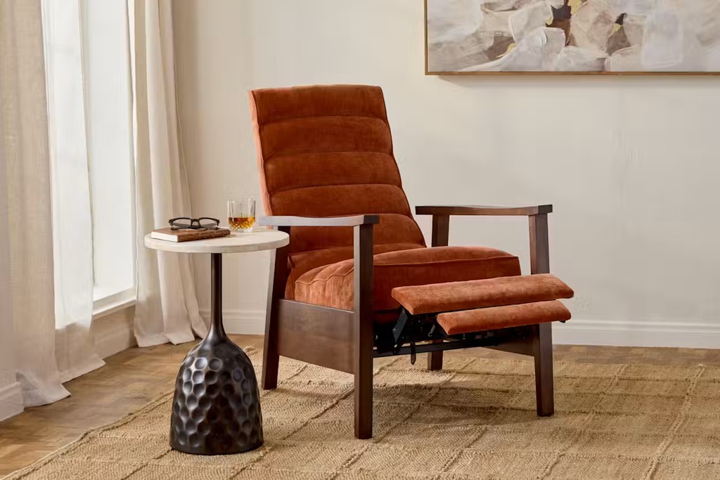 Rust-colored high-back recliner with an extended footrest and wood frame beside a round side table.