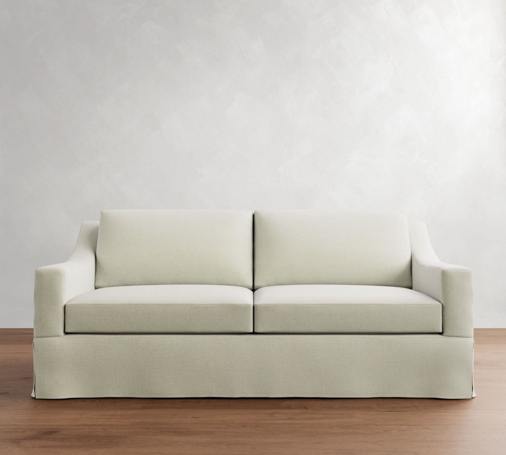 Cream slipcovered sofa with two seat cushions against a white wall and wood floor
