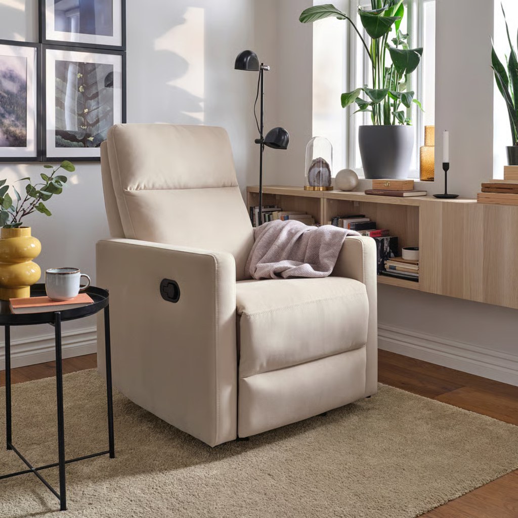 Cream manual bedroom recliner with a throw blanket beside a side table and built-in bookshelf.