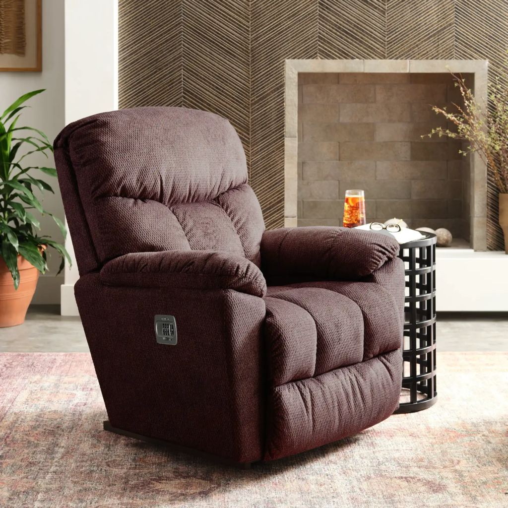 Brown upholstered power recliner beside a round side table and fireplace in a warm living area.