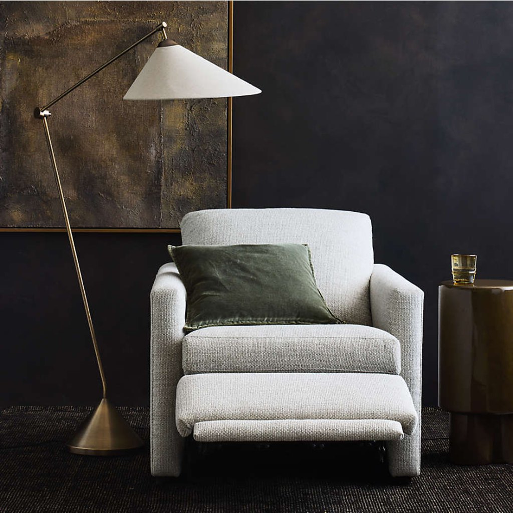 Light gray upholstered power recliner with extended footrest, floor lamp, and side table in a modern reading corner.