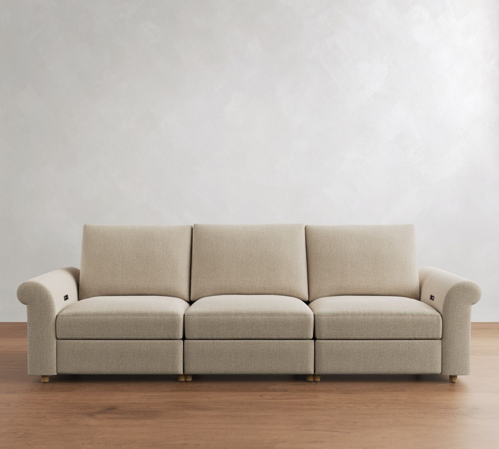 Beige three-seat power reclining sofa with roll arms against a plain white wall on wood flooring.