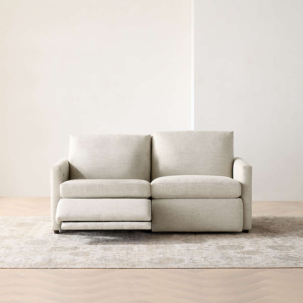 Light gray two-seat power reclining loveseat with one footrest extended on a neutral area rug.