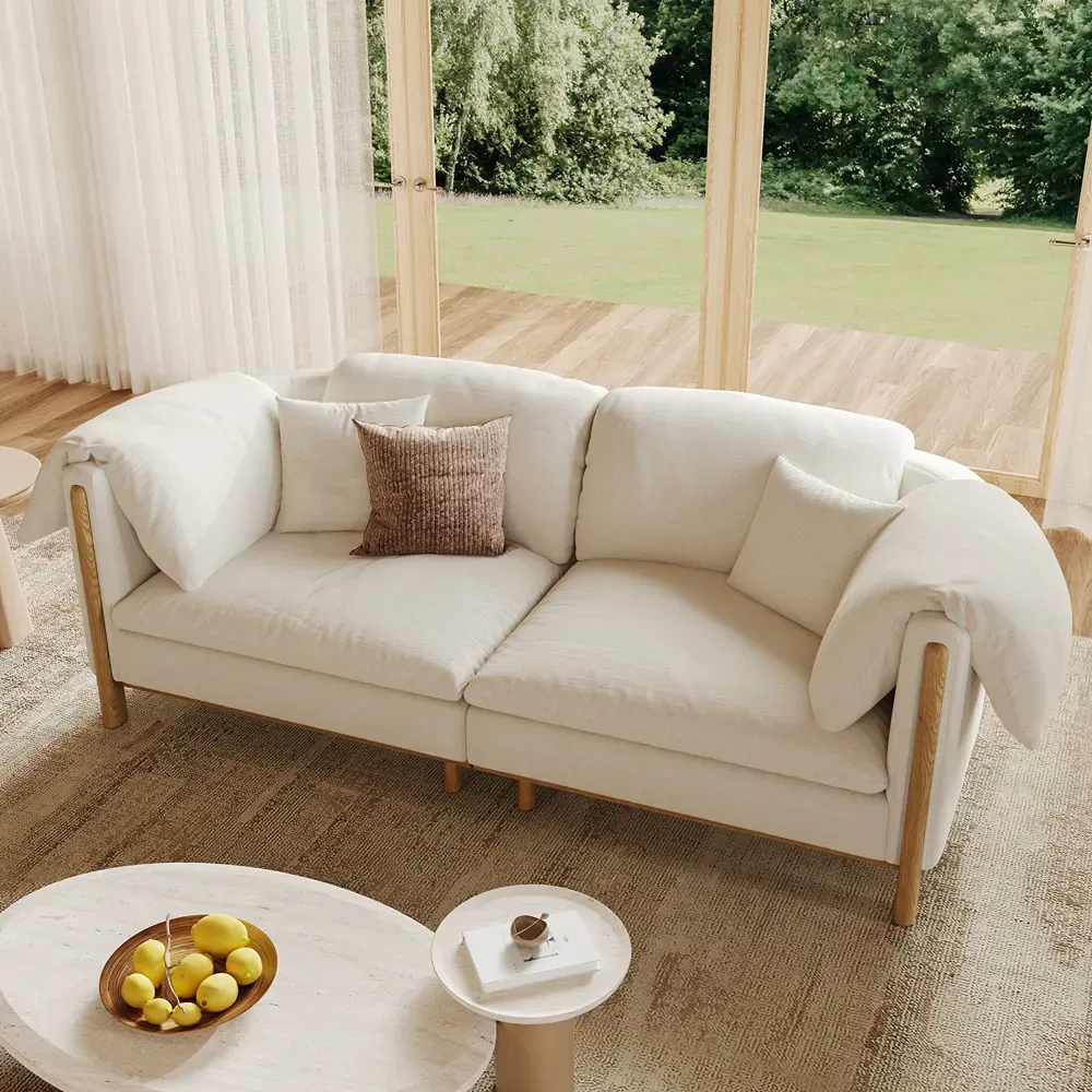 Cream pillow-back sofa with oversized cushions and exposed wood frame in a bright living room.