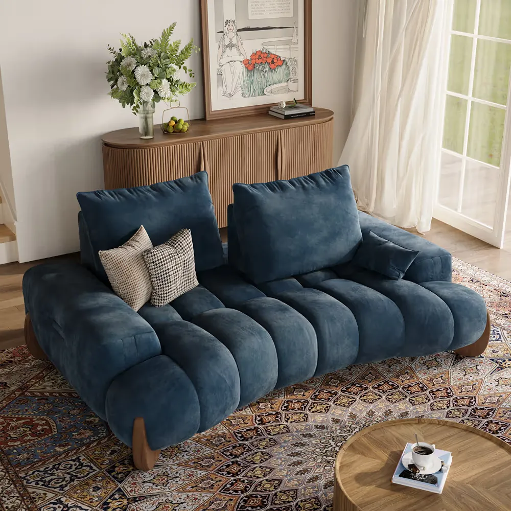 Navy blue velvet sofa with deep cushions in a bright living room with patterned rug and wood cabinet