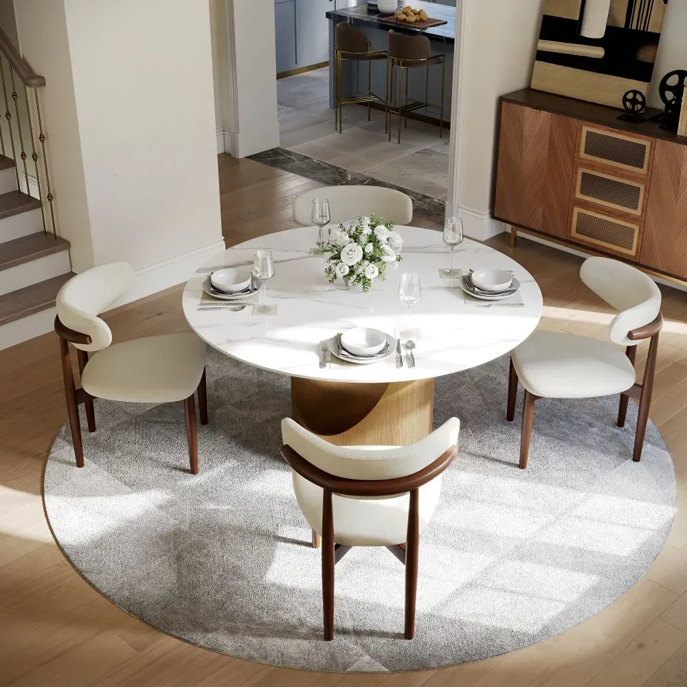 Round dining table with four upholstered chairs in a bright open-plan dining space.
