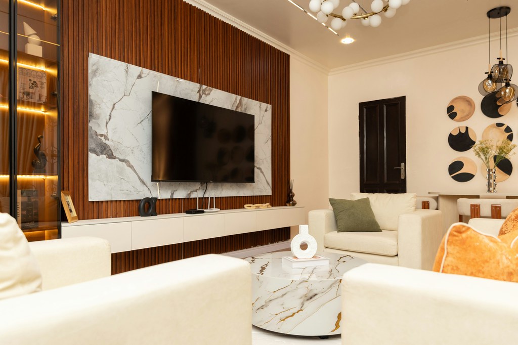 Modern media room with cream seating, marble coffee table, wall-mounted TV, and wood-paneled feature wall.