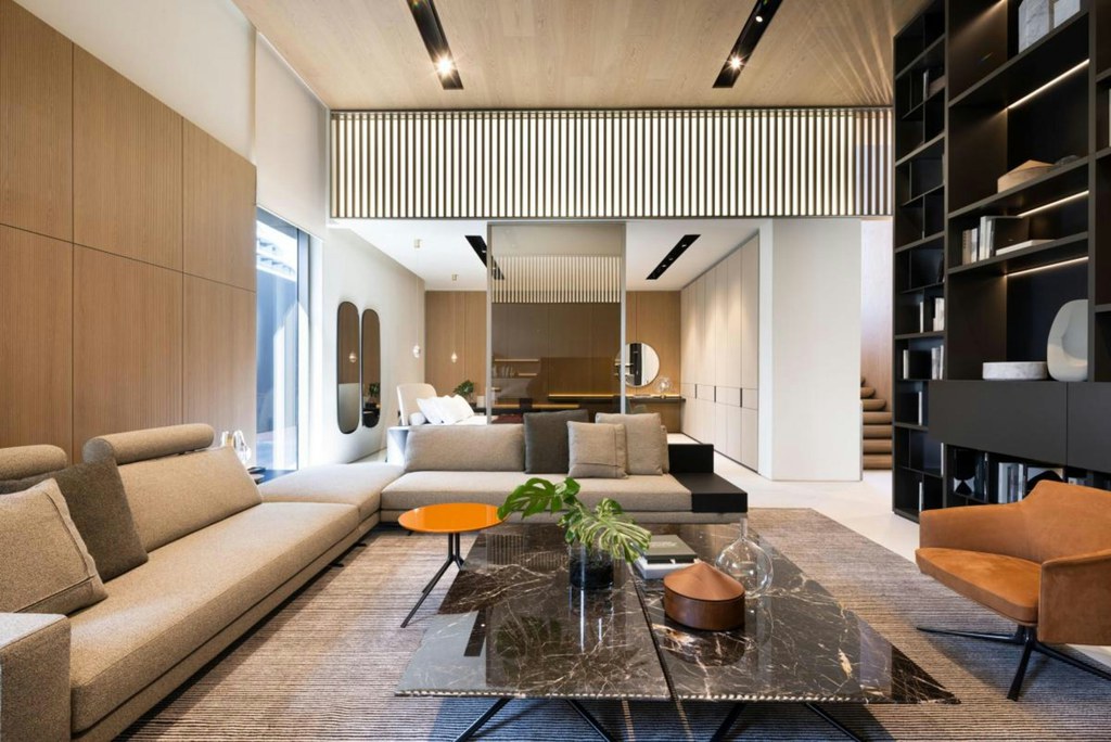 Modern open-plan living room with a large sectional sofa, marble coffee table, built-in shelving, and minimalist contemporary interior design.