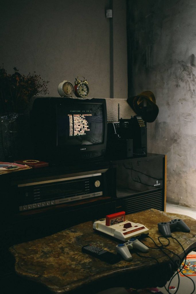 Retro gaming setup with a CRT TV, classic console, cartridge, wired controllers, and vintage audio equipment.