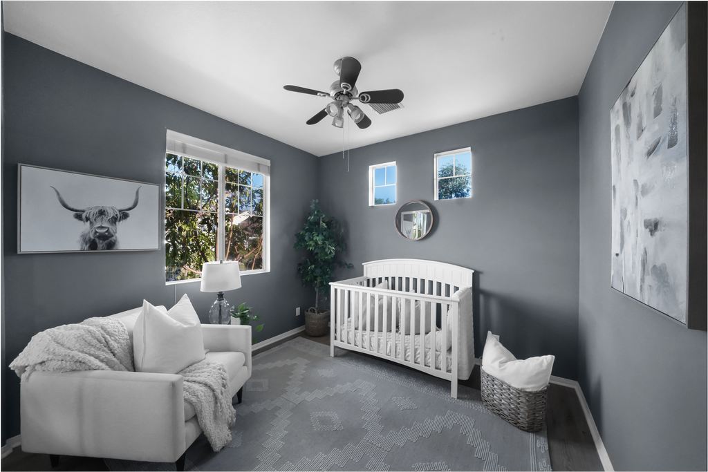 Gray baby nursery with a white crib, upholstered armchair, soft rug, and framed wall art.
