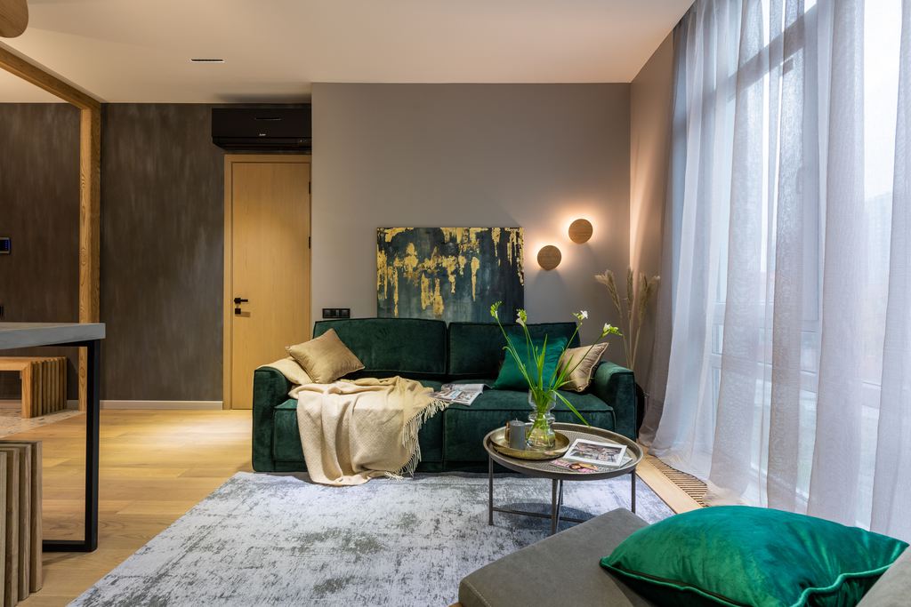 Dark green sofa in a modern living room with a round coffee table, area rug, and floor-to-ceiling windows.