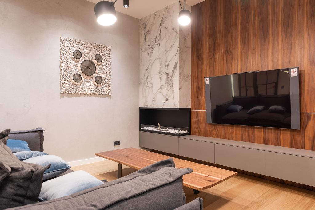 Modern living room with a wall-mounted TV, built-in media console, gray sofa, wooden coffee table, and warm wood accent wall.