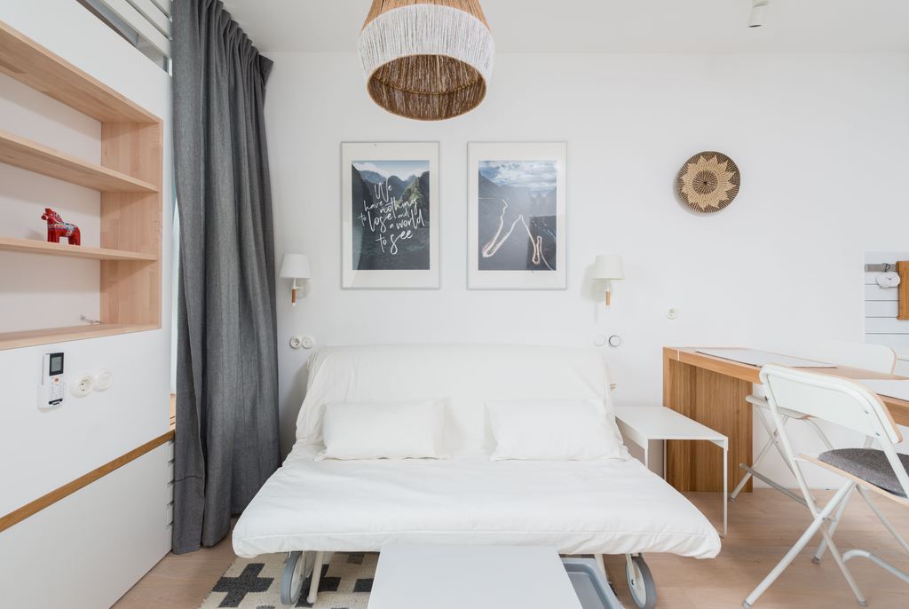 White pull-out sleeper sofa opened in a compact room with a desk, shelving, and wall art.