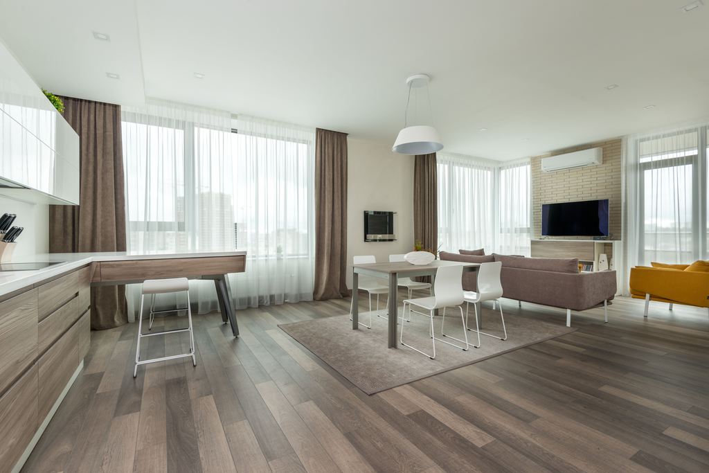 Open-plan living and dining room with sofas, dining chairs, and tables arranged on hardwood flooring.