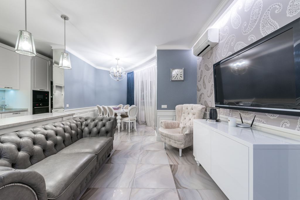 Modern open-plan living room with wall-mounted TV, white media cabinet, sofa seating, and minimalist home entertainment setup.