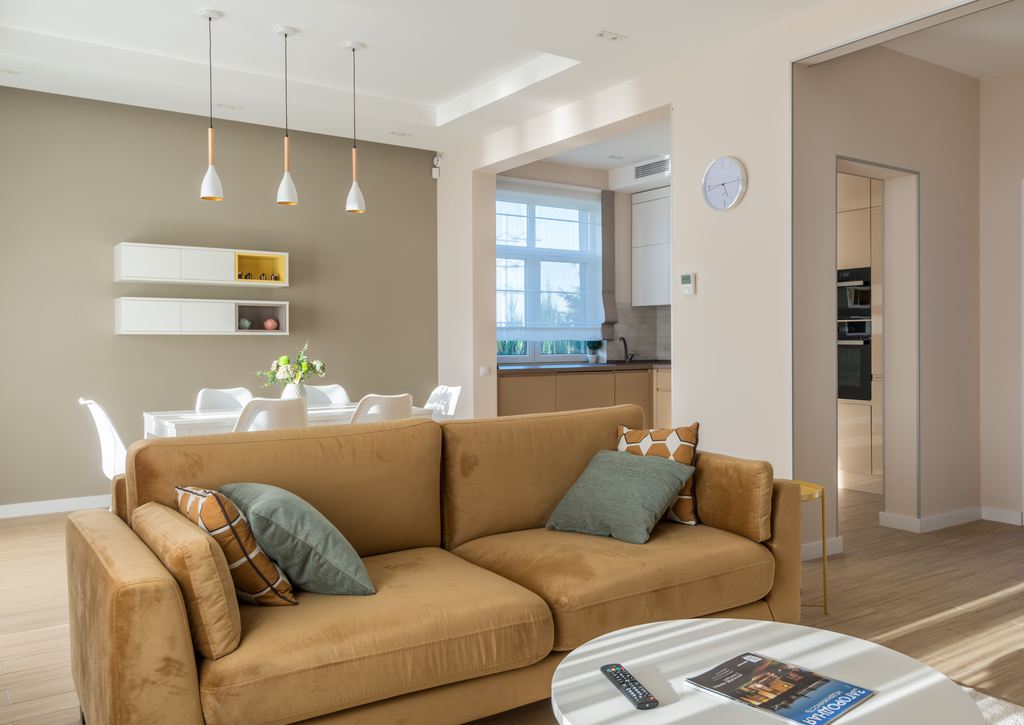 Warm tan sofa with layered cushions in a bright open-plan living and dining room.