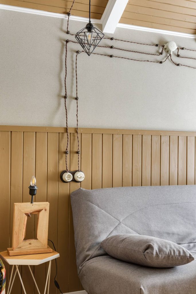 Exposed electrical cords and wall-mounted outlets beside a gray sofa in a living room.