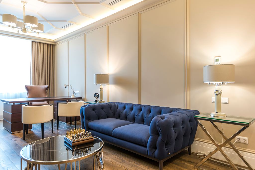 Home office lounge with a large desk, upholstered sofa, side tables, and warm layered lighting.