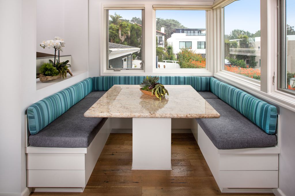 Built-in breakfast nook with upholstered banquette seating and a rectangular dining table beside large windows.