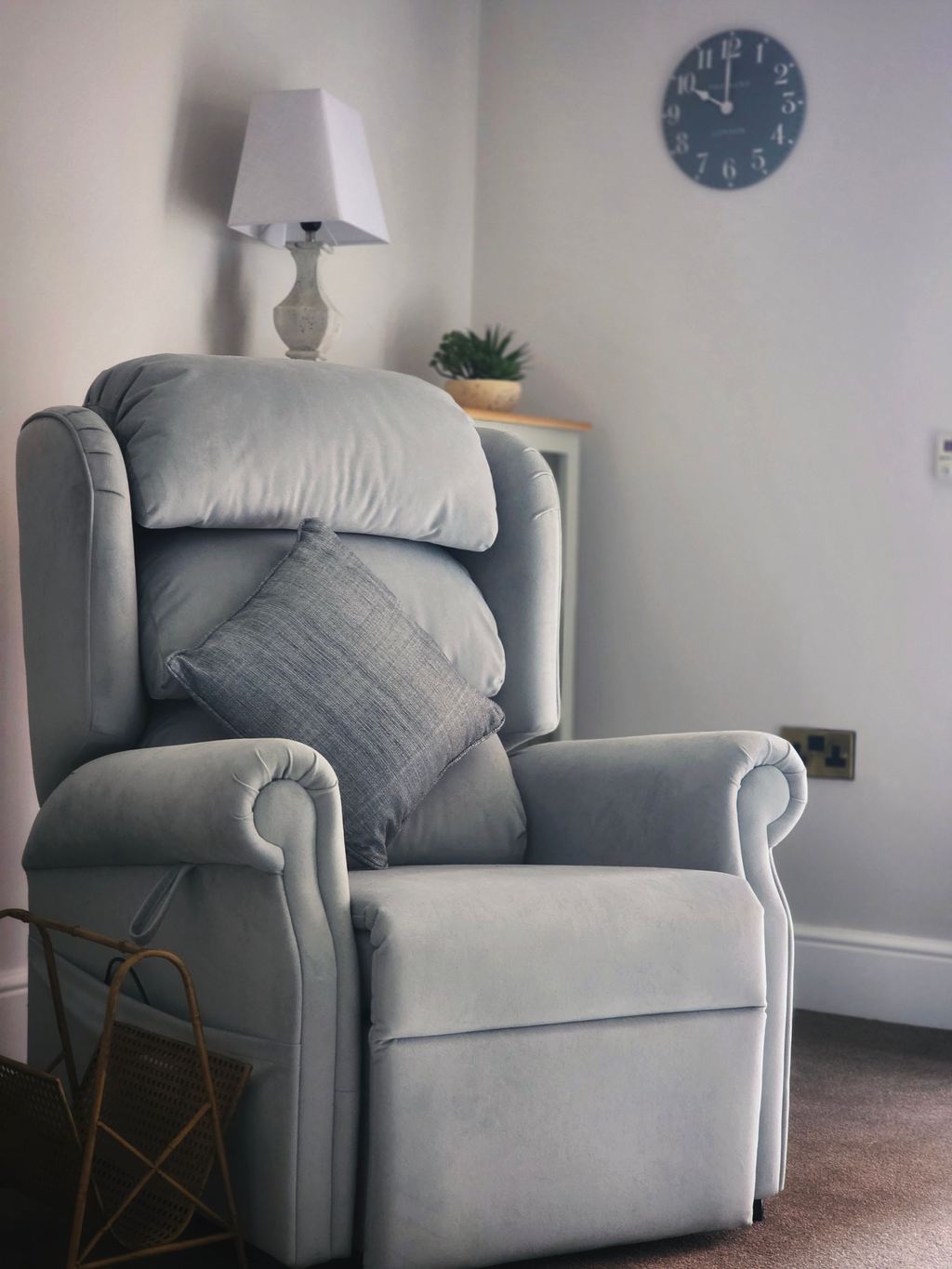 Gray upholstered recliner chair with a cushion in a softly lit living room.
