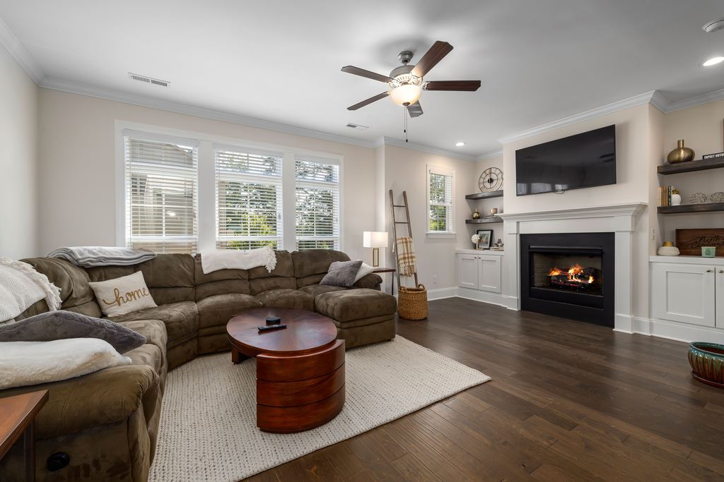 L-shaped sectional sofa arranged beside large windows, facing a wall-mounted TV above a fireplace with a clear walkway.