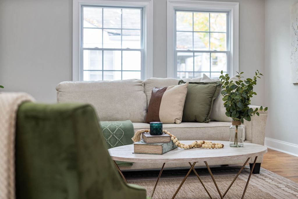 Light and airy living room with a neutral sofa, green accent chair, oval coffee table, plants, and abundant natural light.