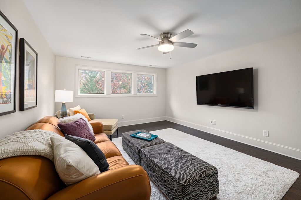 Spacious modern living room with a leather sofa, wall-mounted TV, ottoman coffee table, rug, and minimalist home theater setup.