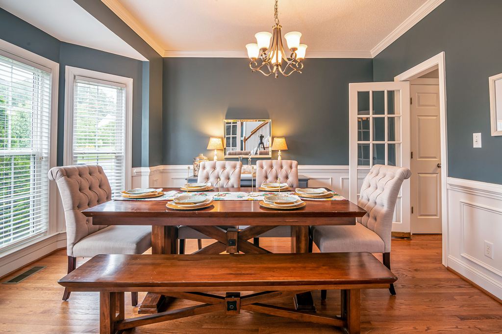 Wooden dining table with upholstered chairs and a matching bench in a bright traditional dining room.