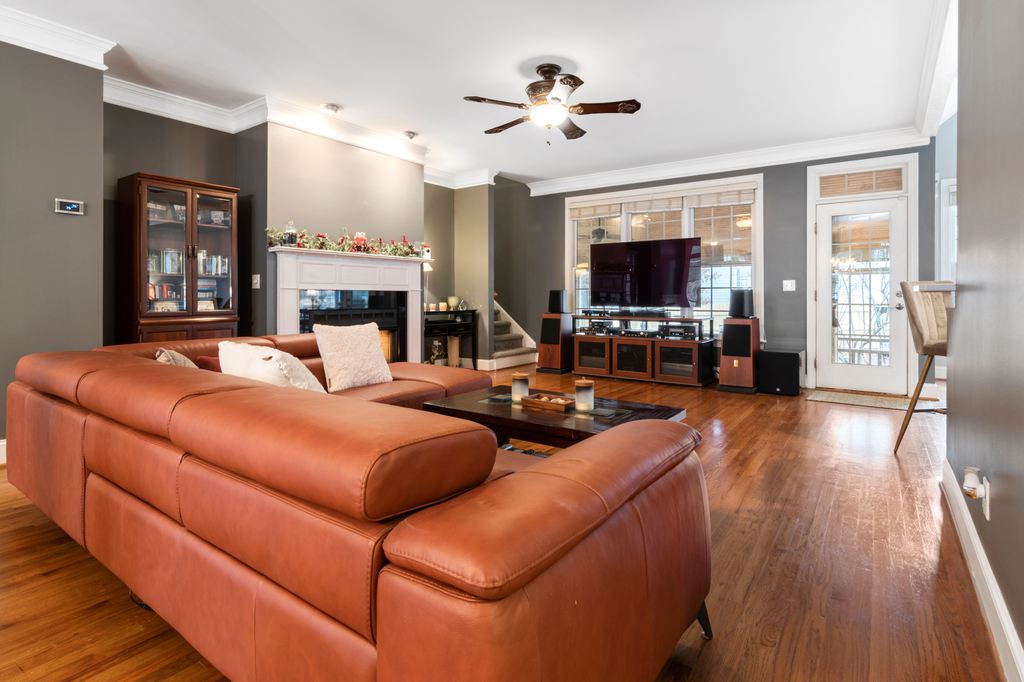 Brown leather sectional sofa in a spacious living room with hardwood floors, fireplace, TV, and large windows.