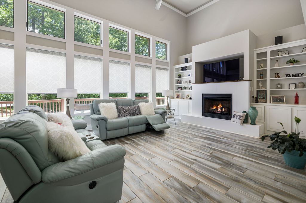 Light green reclining sofas facing a TV and fireplace in a bright living room with large windows.