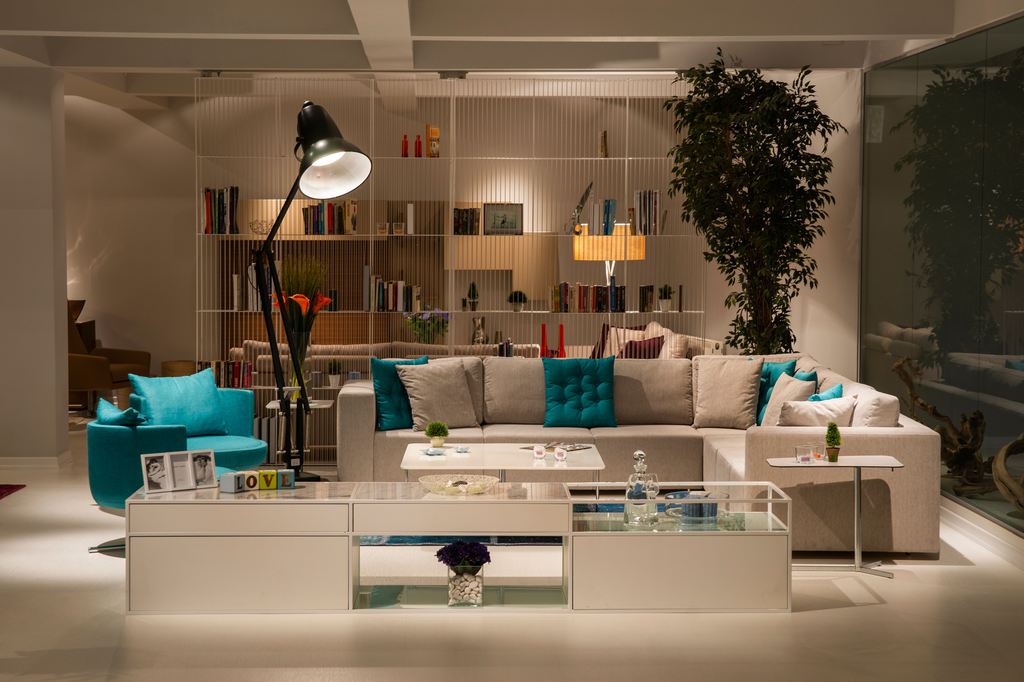 Beige L-shaped sectional sofa with turquoise accent pillows, paired with an armchair and low tables in a modern open living room.