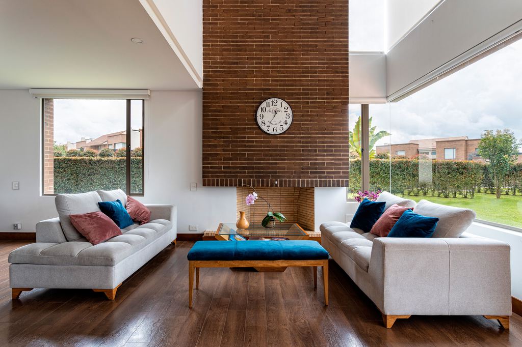 Two light gray tufted bench-seat sofas facing a brick fireplace in a bright modern living room.