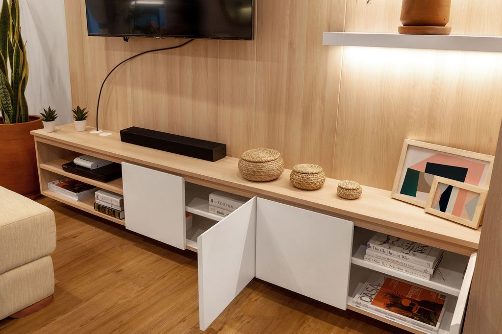 Light wood TV stand with open cabinet doors, wall-mounted TV, soundbar, books, and media storage in a modern living room.