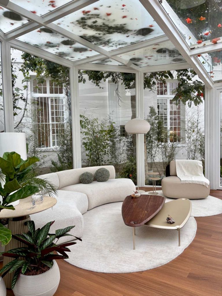 Curved white sectional sofa with organic nesting coffee tables in a bright sunroom.