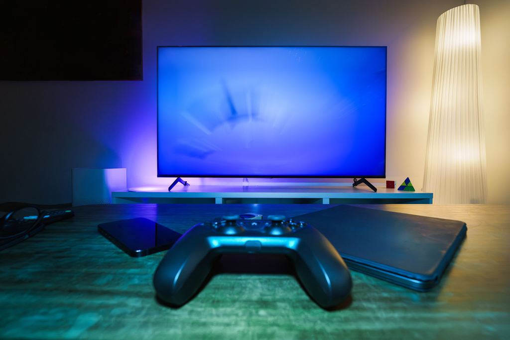 Gaming controller on a table in front of a TV and low media console with blue ambient lighting.