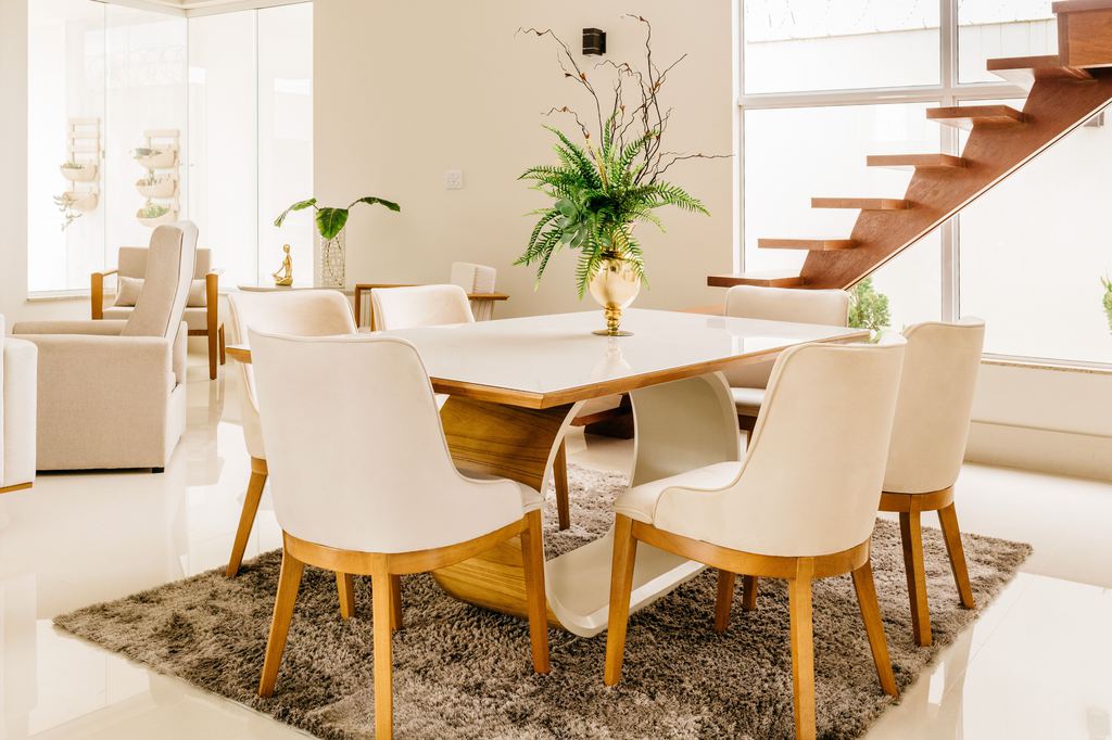 Modern white dining table with six upholstered chairs in a bright open-plan dining room.