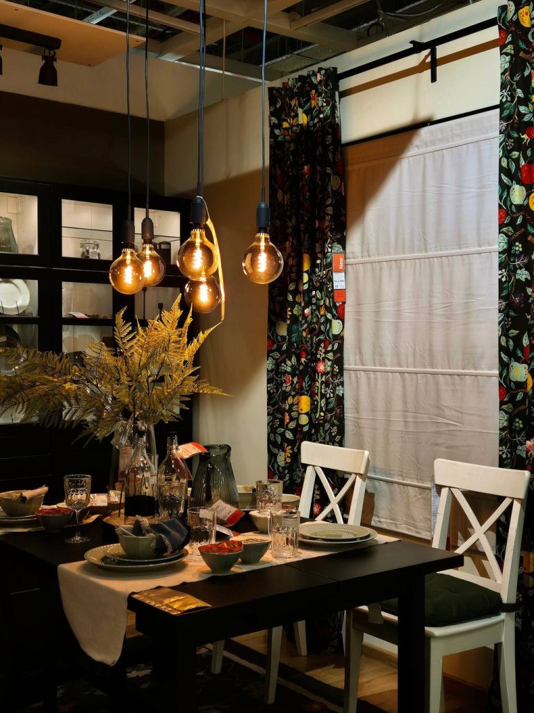 Black rectangular dining table with white cross-back chairs under exposed-bulb pendant lights.