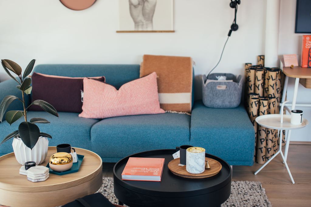 Two round drum coffee tables in wood and black finishes placed in front of a blue sofa in a colorful living room.