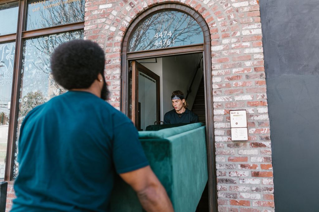Two movers carrying a green sofa through a narrow doorway.