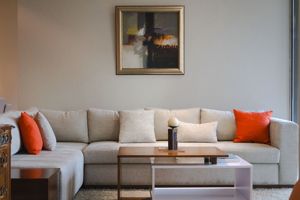White L-shaped sectional sofa with a chaise, layered coffee tables, and orange accent pillows in a modern living room.