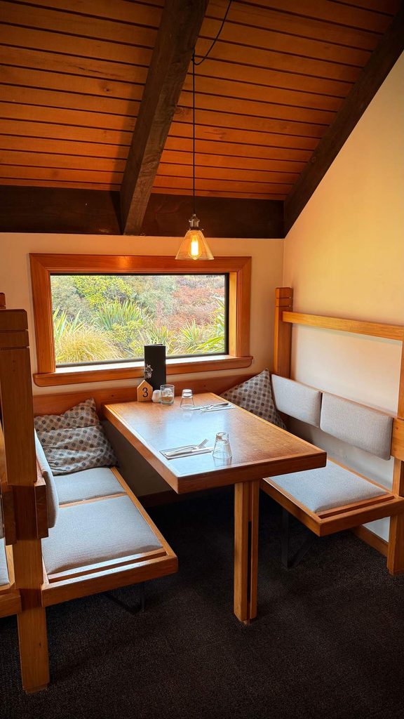 Cozy wooden dining nook with built-in bench seating and a rectangular table beside a large window.
