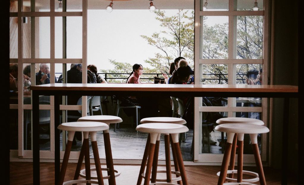 Wooden bar stools lined up at a café counter with diners seated in the background.