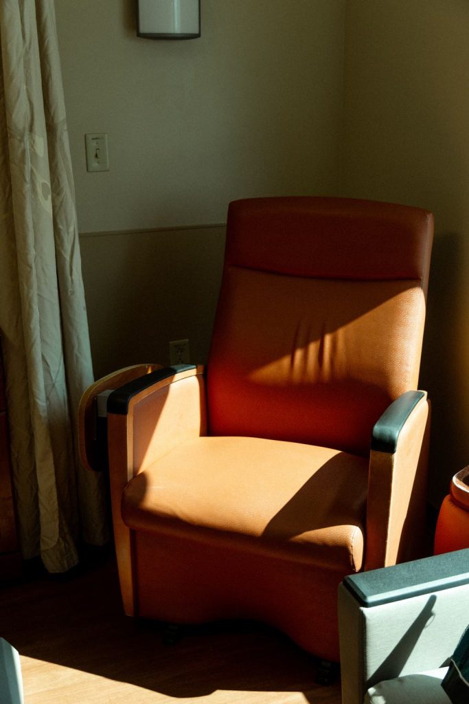 Orange-brown leather recliner chair in warm sunlight beside a window curtain