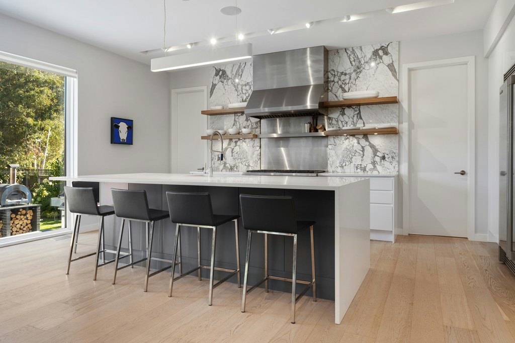 Modern white kitchen island with four black counter stools on metal frames.