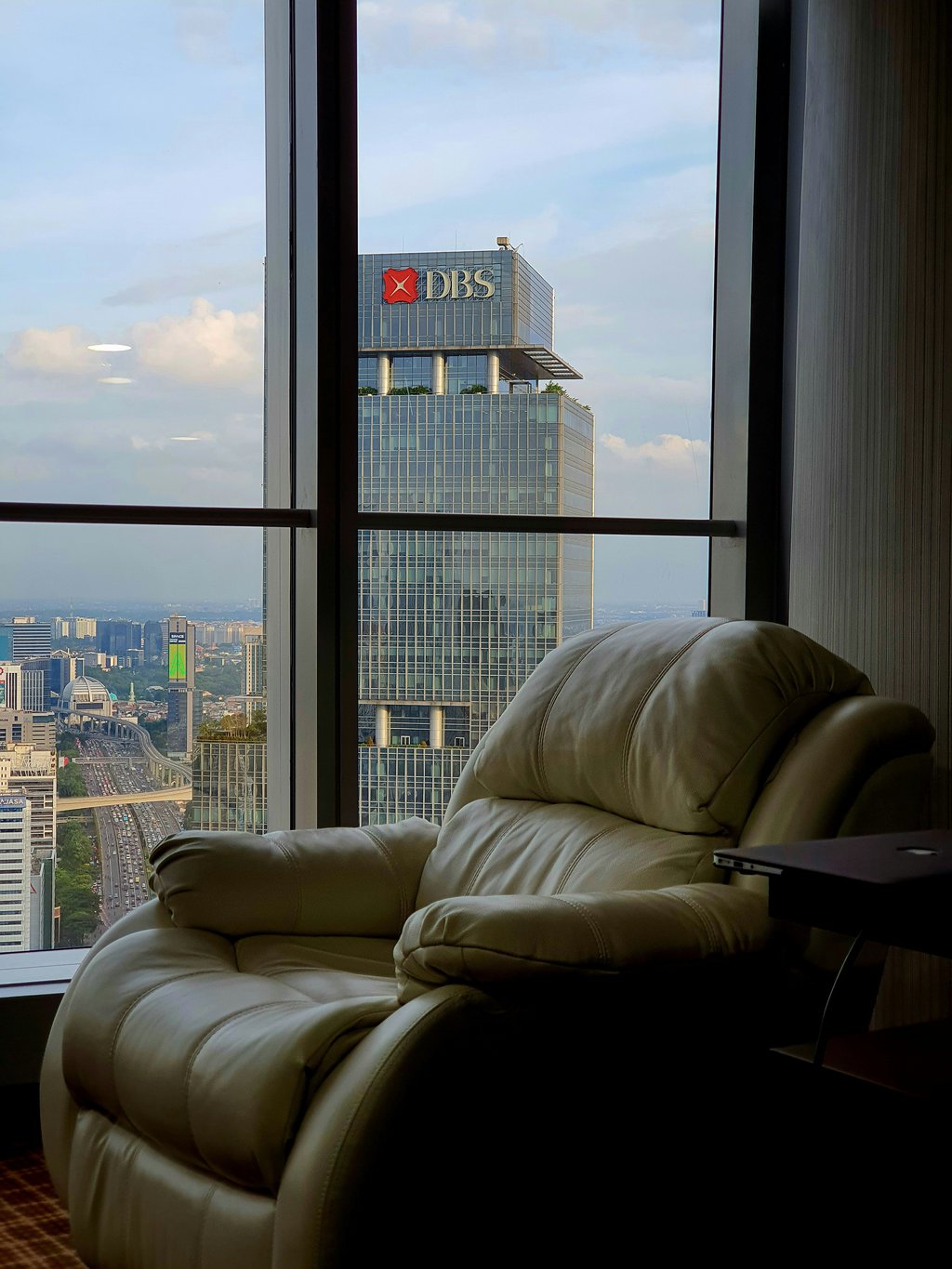 Leather recliner chair beside a floor-to-ceiling window overlooking a city skyline