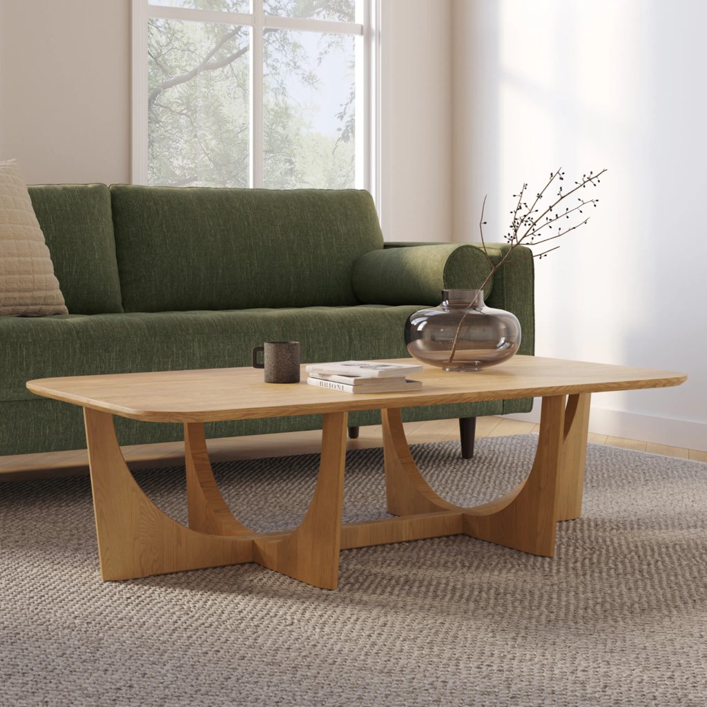 Large rectangular oak coffee table with curved legs in front of a green sofa in a bright modern living room.