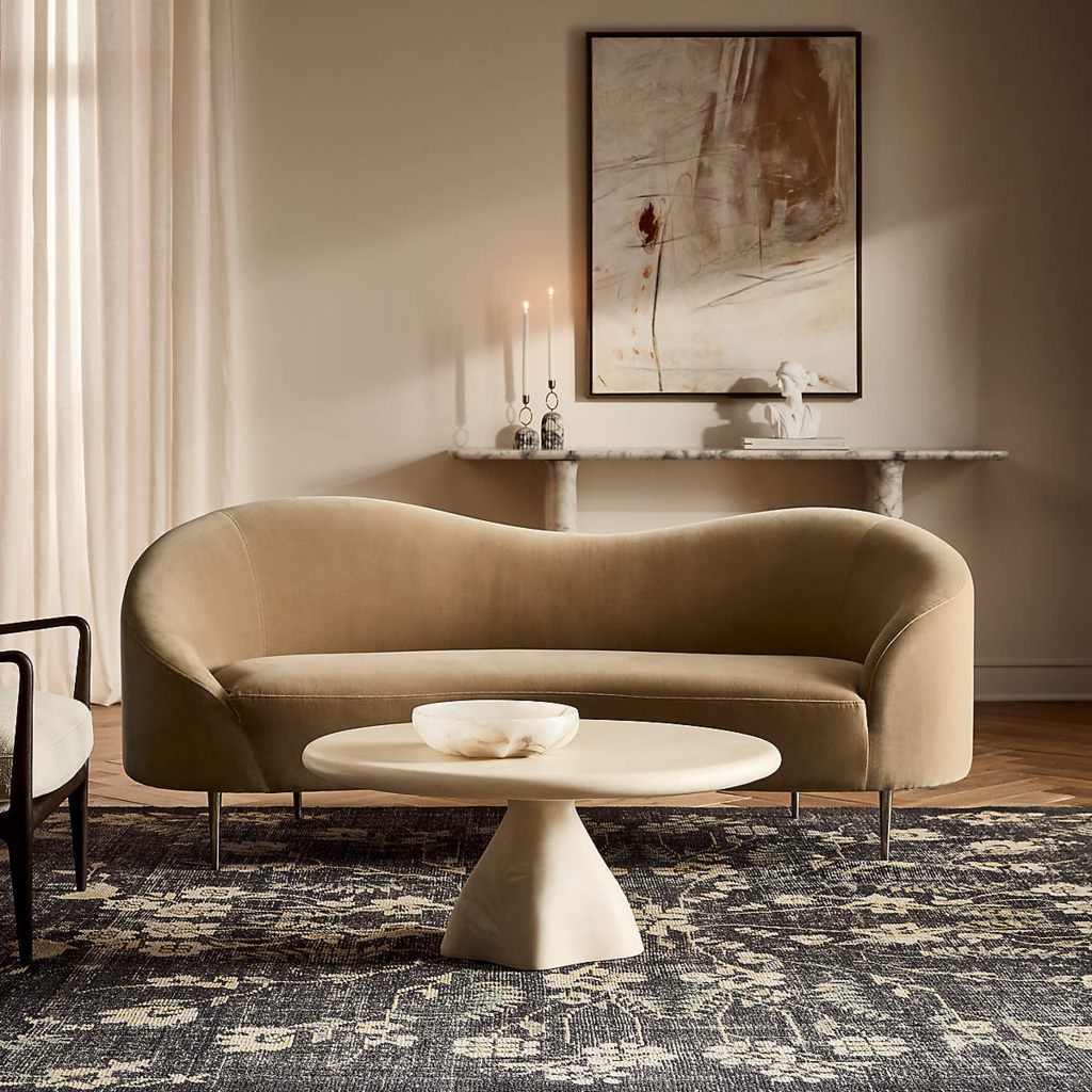 Large round pedestal coffee table in front of a curved beige sofa in an elegant neutral living room.