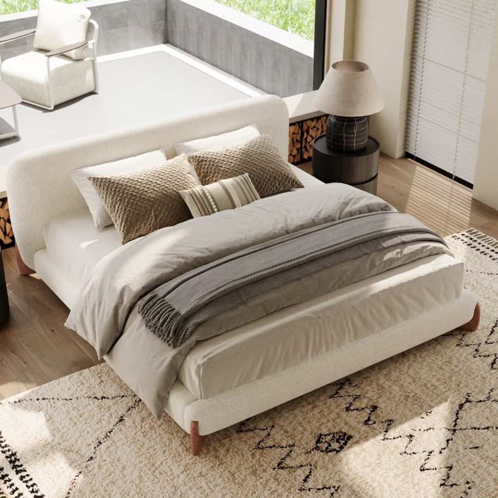 Beige upholstered bed with layered neutral bedding in a bright modern bedroom.